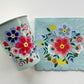 The Blossom Party Kit paper party napkins and paper cups. The flower/floral pattern includes green, red and blue colours. The napkins have scalloped edges.