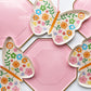 A large pink and gold paper party plate and a small butterfly shaped paper party plate. The Butterfly pattern includes pink, gold, blue, green and orange colours. The large party plates are in the shape of an octagon.