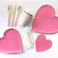 The complete Pink Heart Party Kit including large heart shaped paper party plates, small heart shaped paper party plates, pink and white heart patterned paper cups, heart shaped paper napkins, pink dipped wooden utensils and tall white glitter birthday candles. The Blush pattern features bright pink and gold foil colours. 