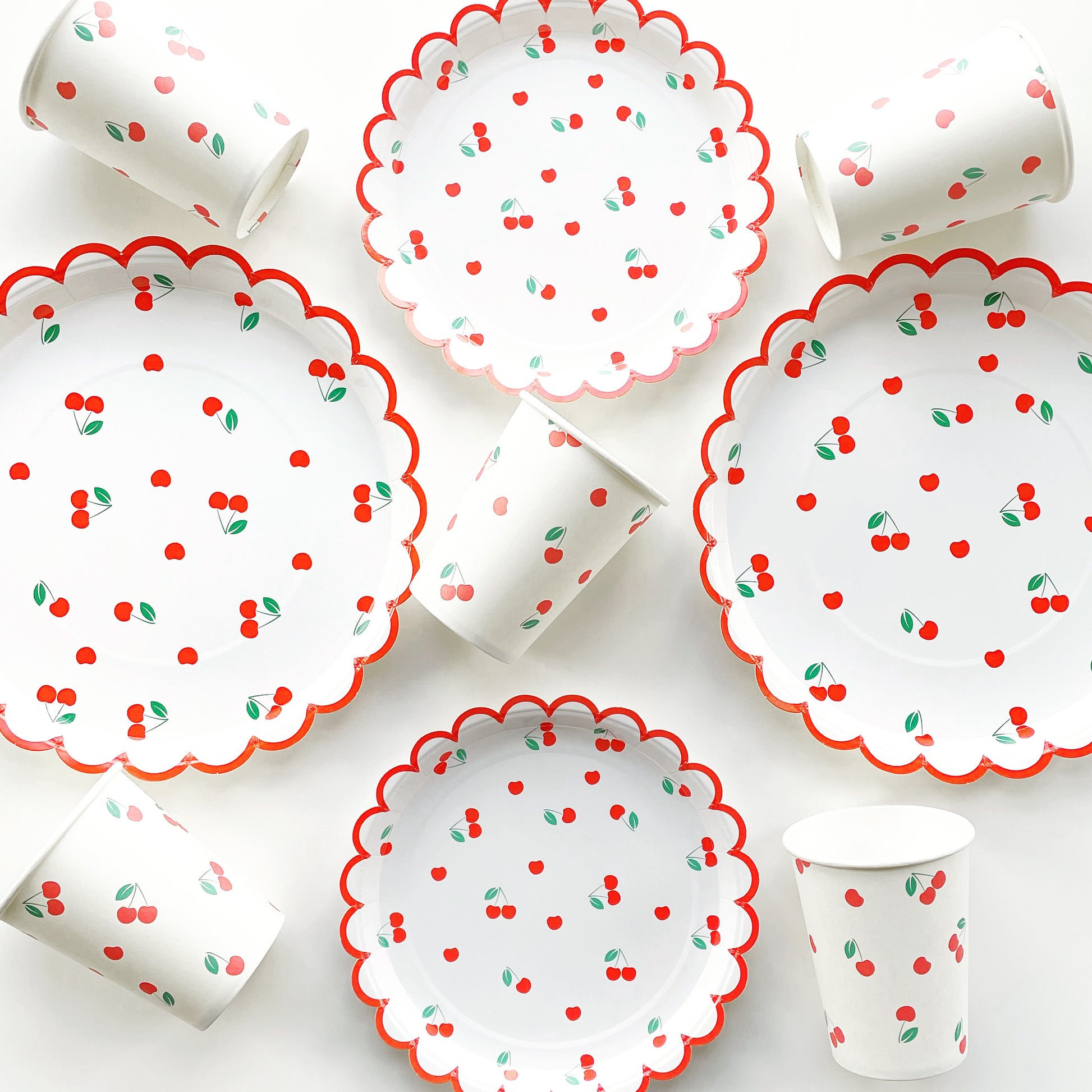 Parts of the Cherry Party Kit including large paper party plates, small paper party plates and paper cups. The cherry party kit features a red, green and white cherry print. The party plates feature red scalloped edges.
