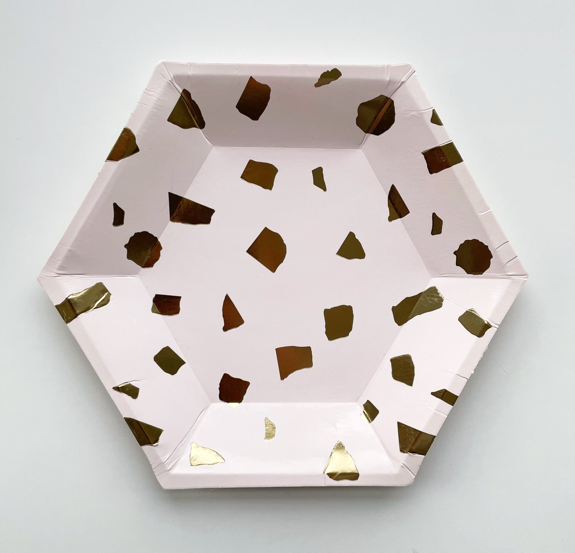 The large paper party plates are in the shape of a hexagon. The plates are a pale blush pink colour with gold foil detail.