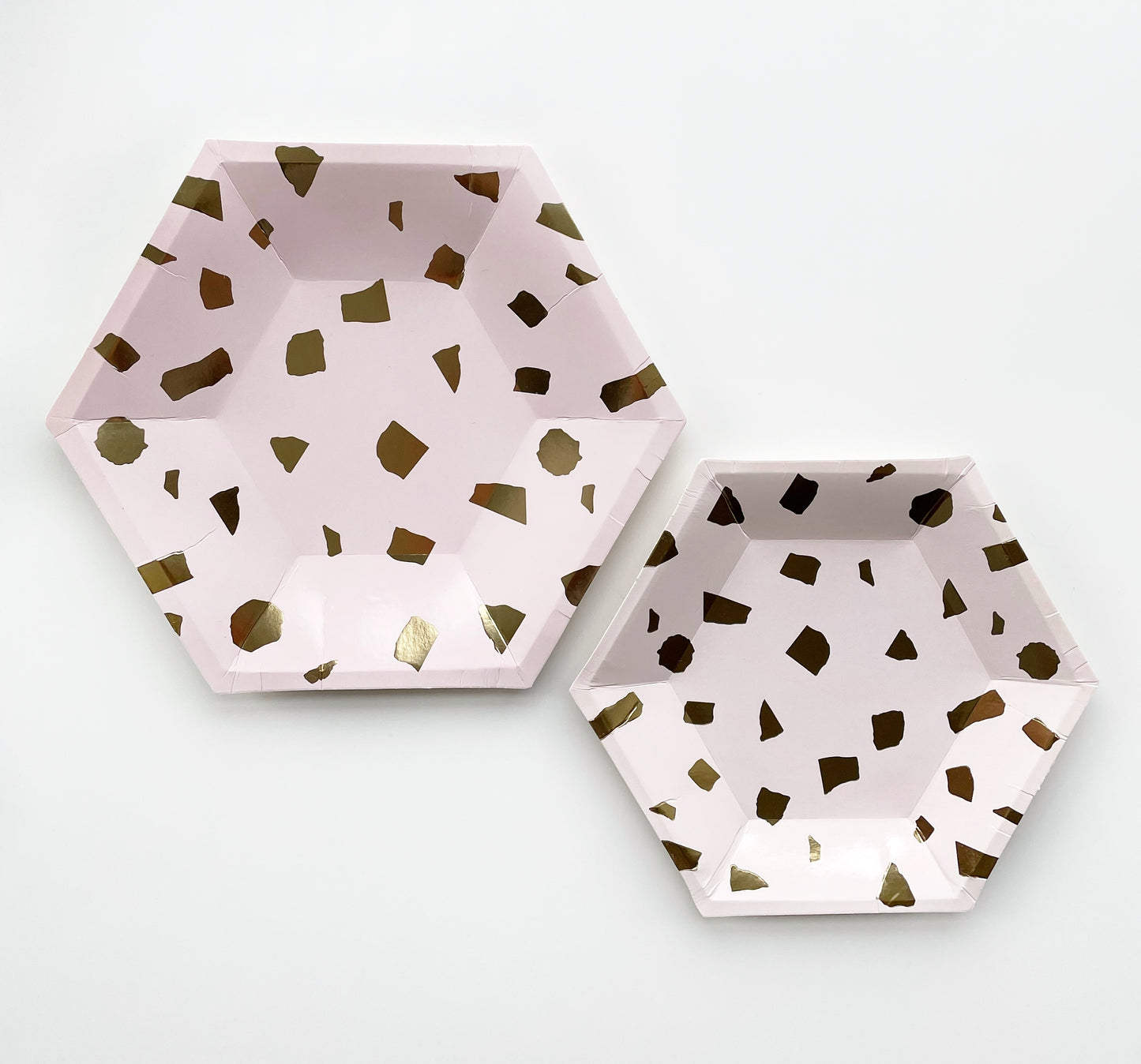 The large and small paper party plates are in the shape of a hexagon. The plates are a pale blush pink colour with gold foil detail.