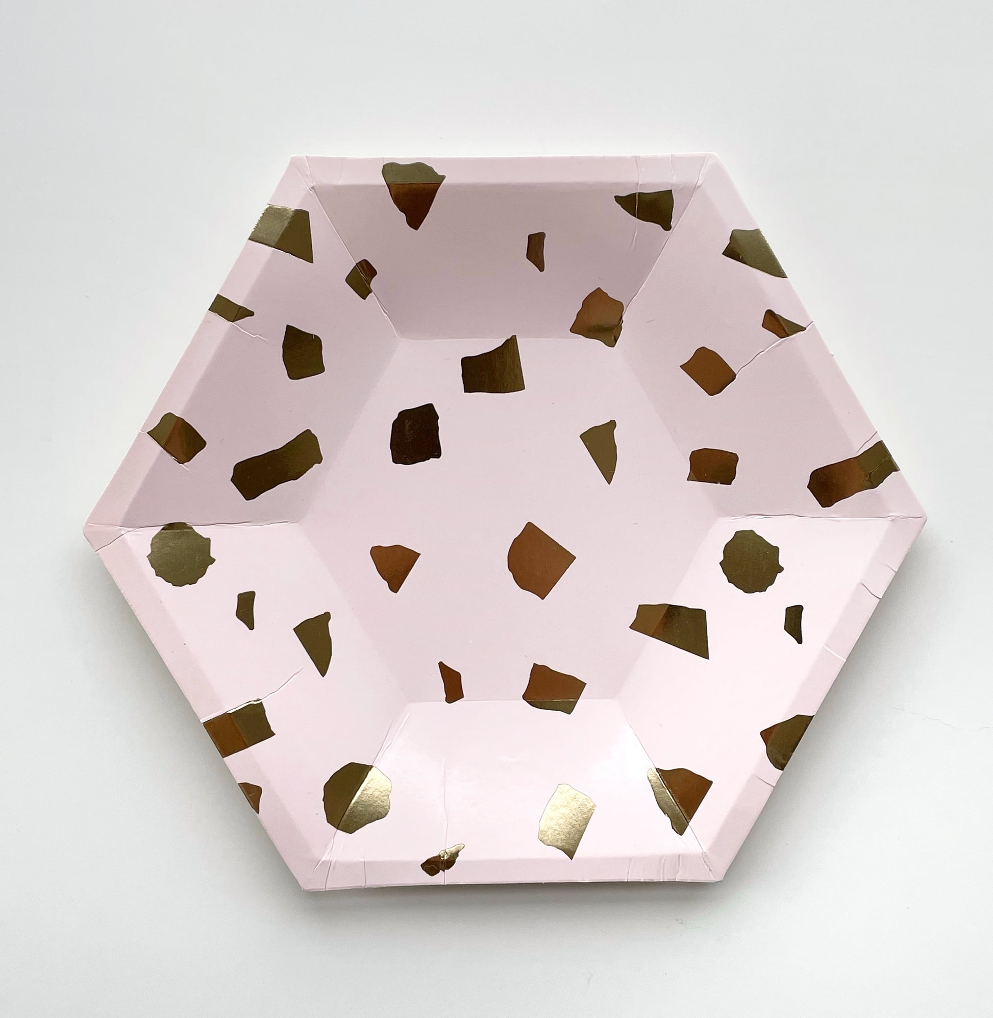 The small paper party plates are in the shape of a hexagon. The plates are a pale blush pink colour with gold foil detail.