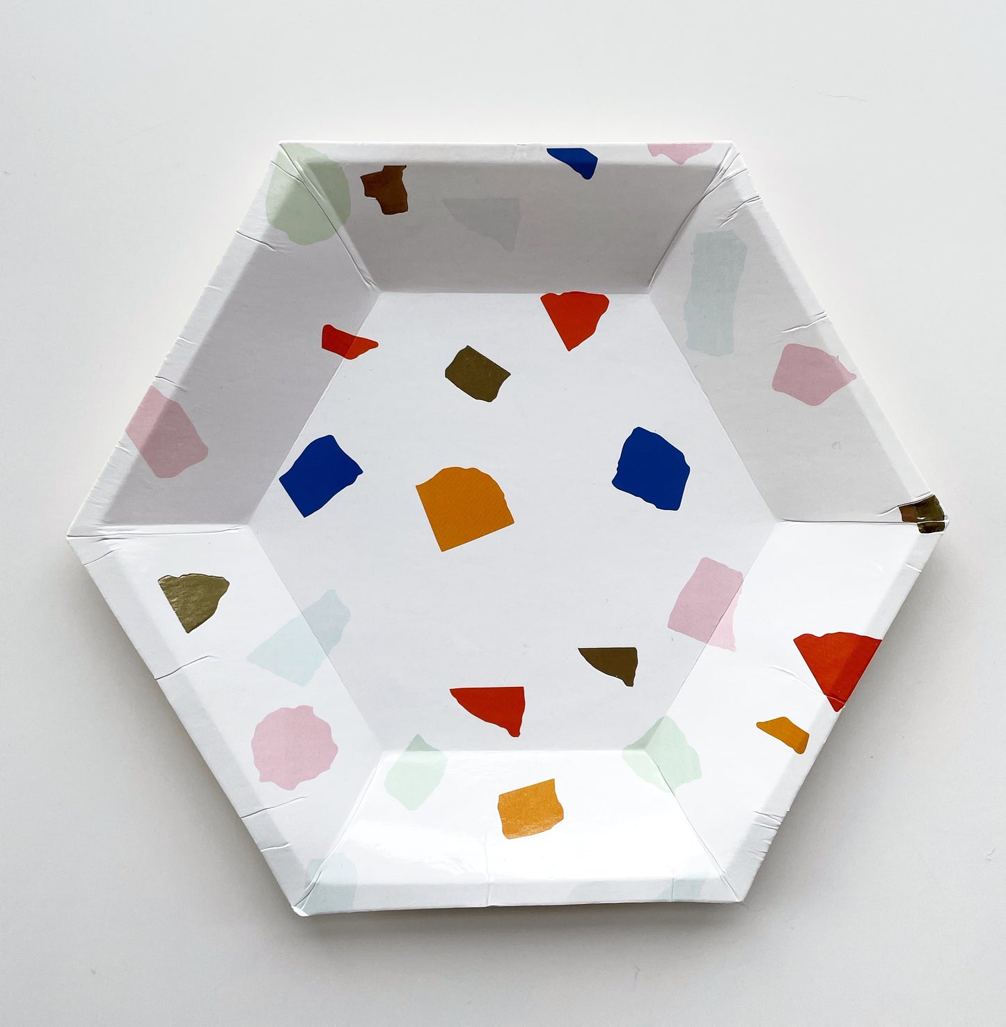  The small Terrazzo paper party plates are in the shape of a hexagon. The terrazzo pattern includes blue, gold, orange and green colours.  