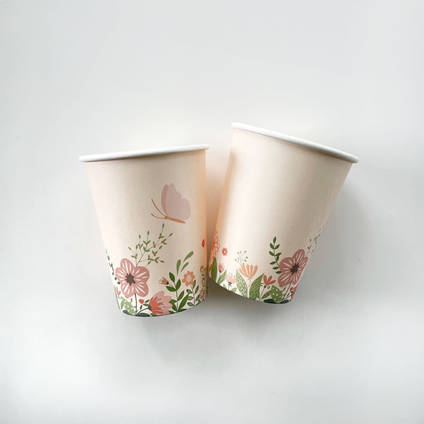 Two paper party cups with a flower and butterfly pattern in the colours pink and green.