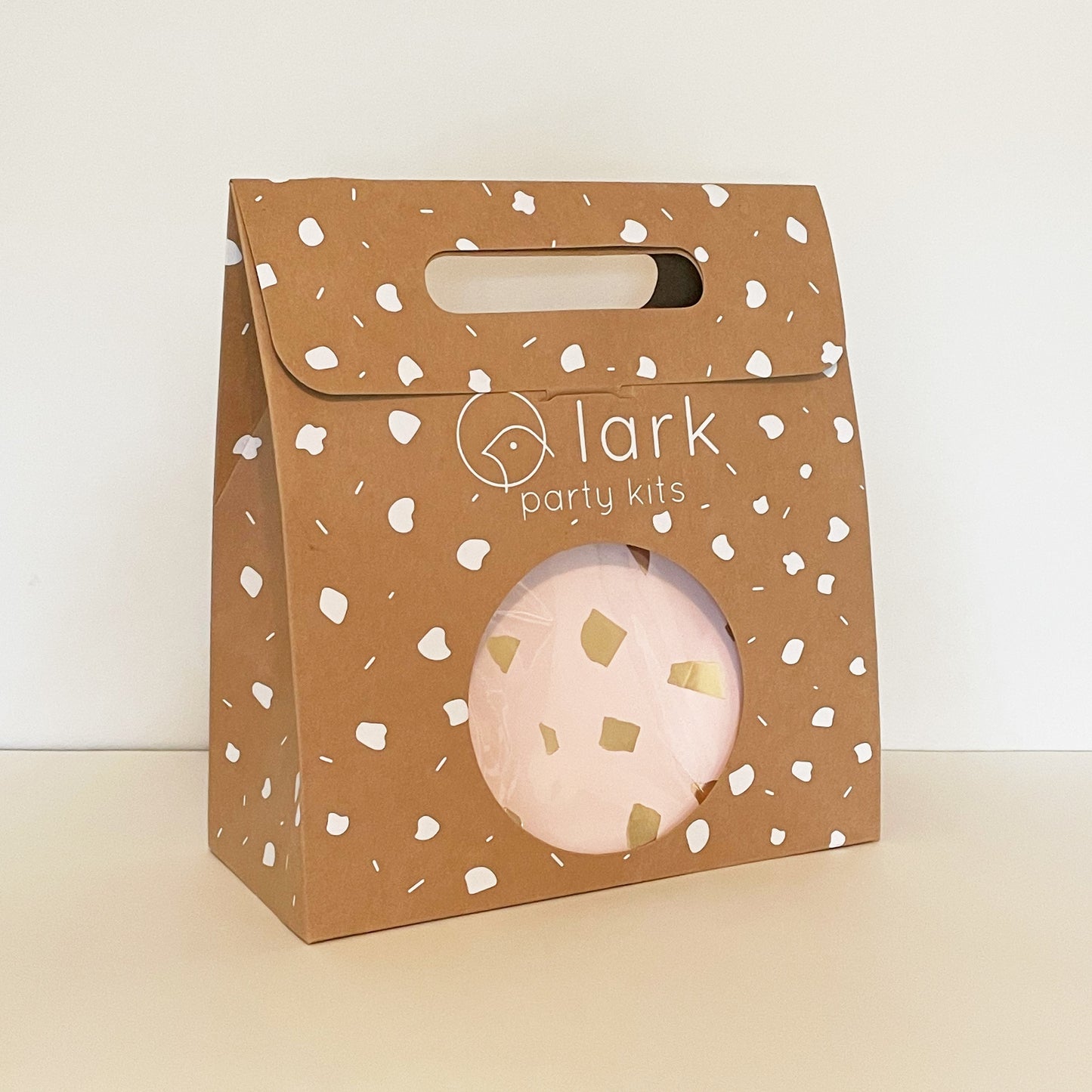The Blush Party Kit in its kraft brown and white carry box. The box features a handle and a circular opening where you can see the contents inside.