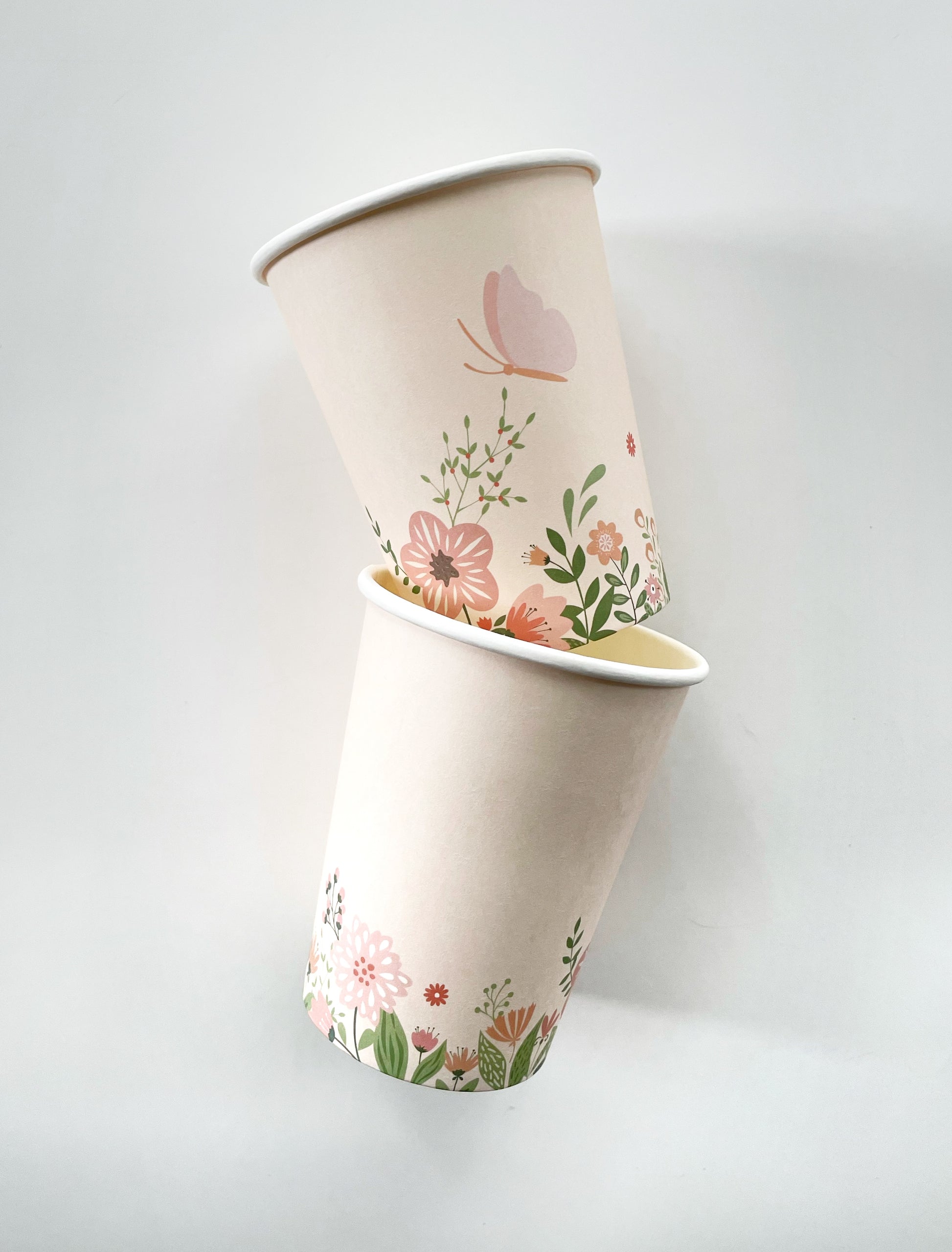 Two paper party cups with a flower and butterfly pattern in the colours pink and green.