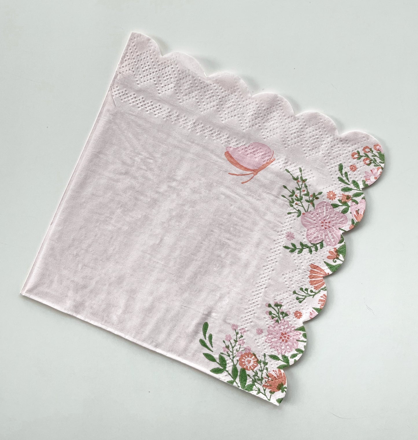 A paper party cocktail napkin with a flower and butterfly pattern in the colours pink and green.