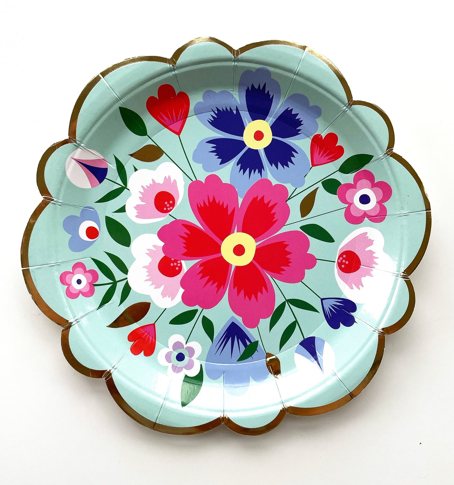 The Blossom Party Kit's paper party plates. The flower/floral pattern includes green, red and blue colours. The party plates have gold scalloped edges.