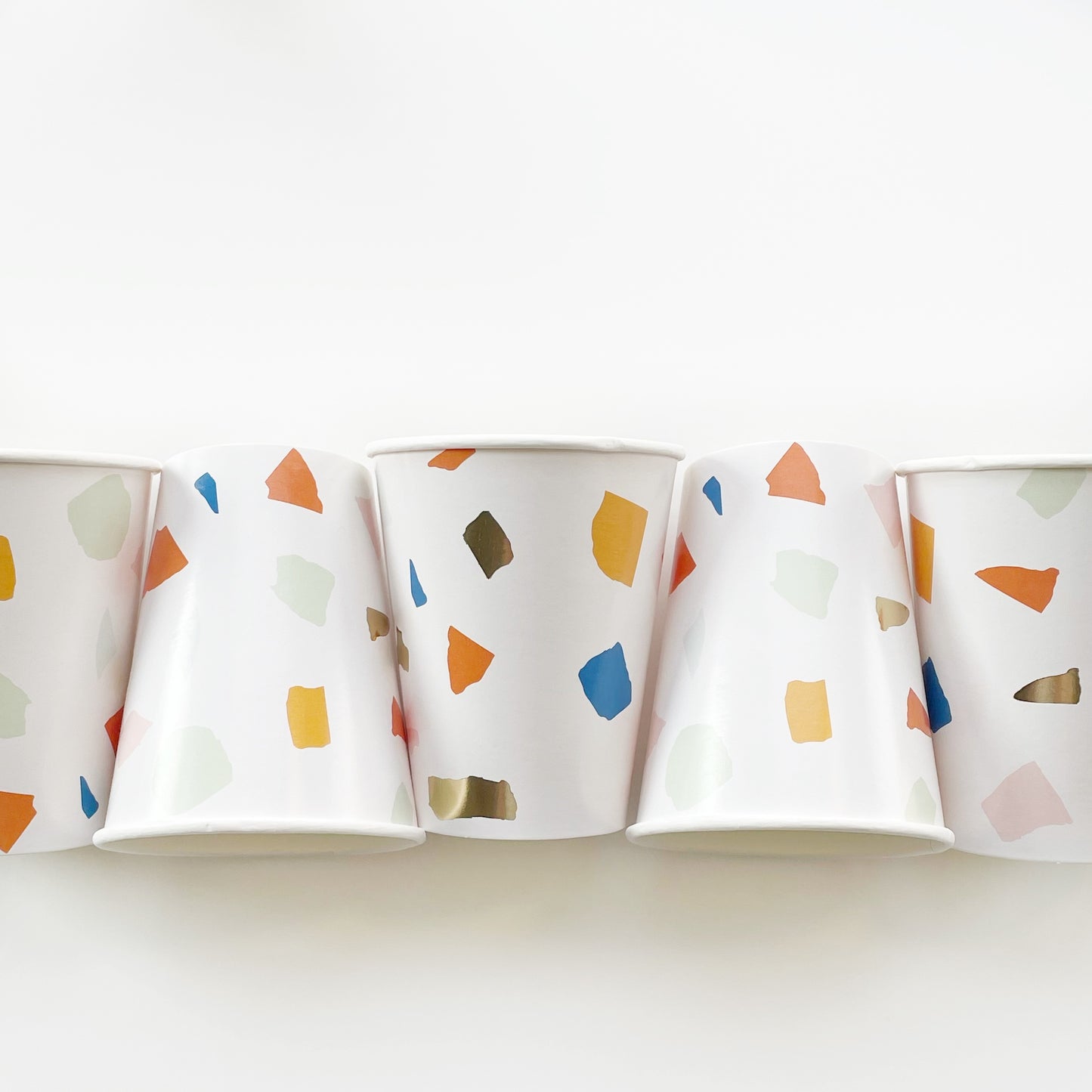 A row of paper party cups featuring a terrazzo pattern including blue, orange and green colours with gold foil detail.