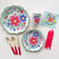 The complete Blossom Party Kit including large paper party plates, small paper party plates, paper cups, paper napkins, red dipped wooden utensils and tall red birthday candles. The flower/floral pattern includes green, red and blue colours. The party plates have gold scalloped edges.
