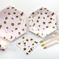 The complete Blush Party Kit including large paper party plates, small paper party plates, paper cups, paper napkins, gold dipped wooden utensils and tall white glitter birthday candles. The Blush pattern features pale blush pink and gold foil colours. The party plates are in the shape of a hexagon. The napkins have a scalloped edge.