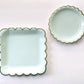 The large and small paper party plates. The plates are a pale pastel blue colour with gold foil scalloped trim.
