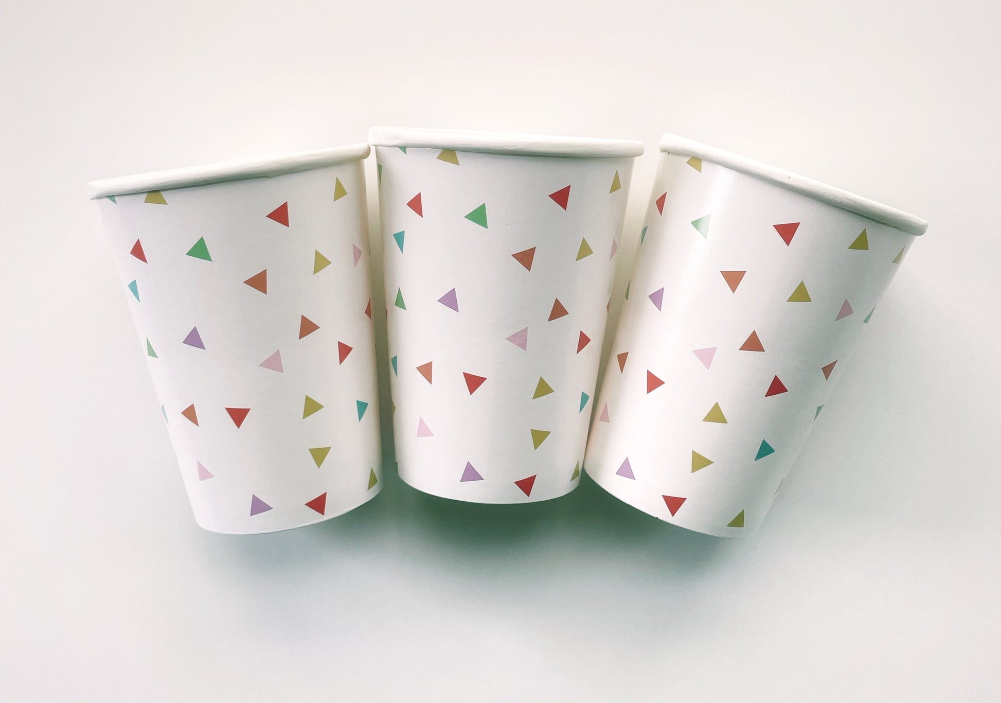 Paper party cups with a triangle pattern featuring green, orange, pink, blue and yellow colours.