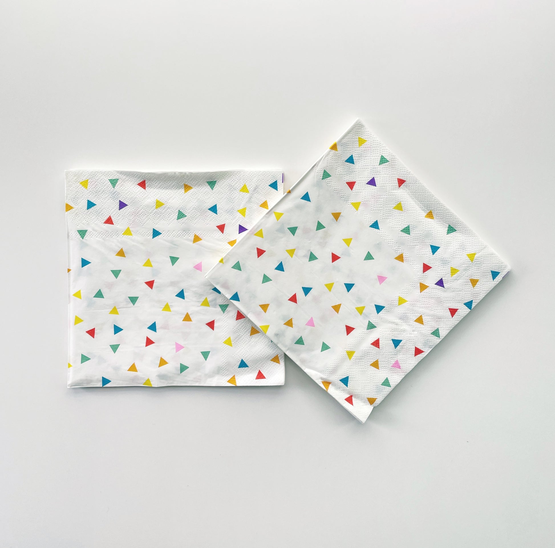 Paper party napkins with a triangle pattern featuring green, orange, pink, blue and yellow colours.