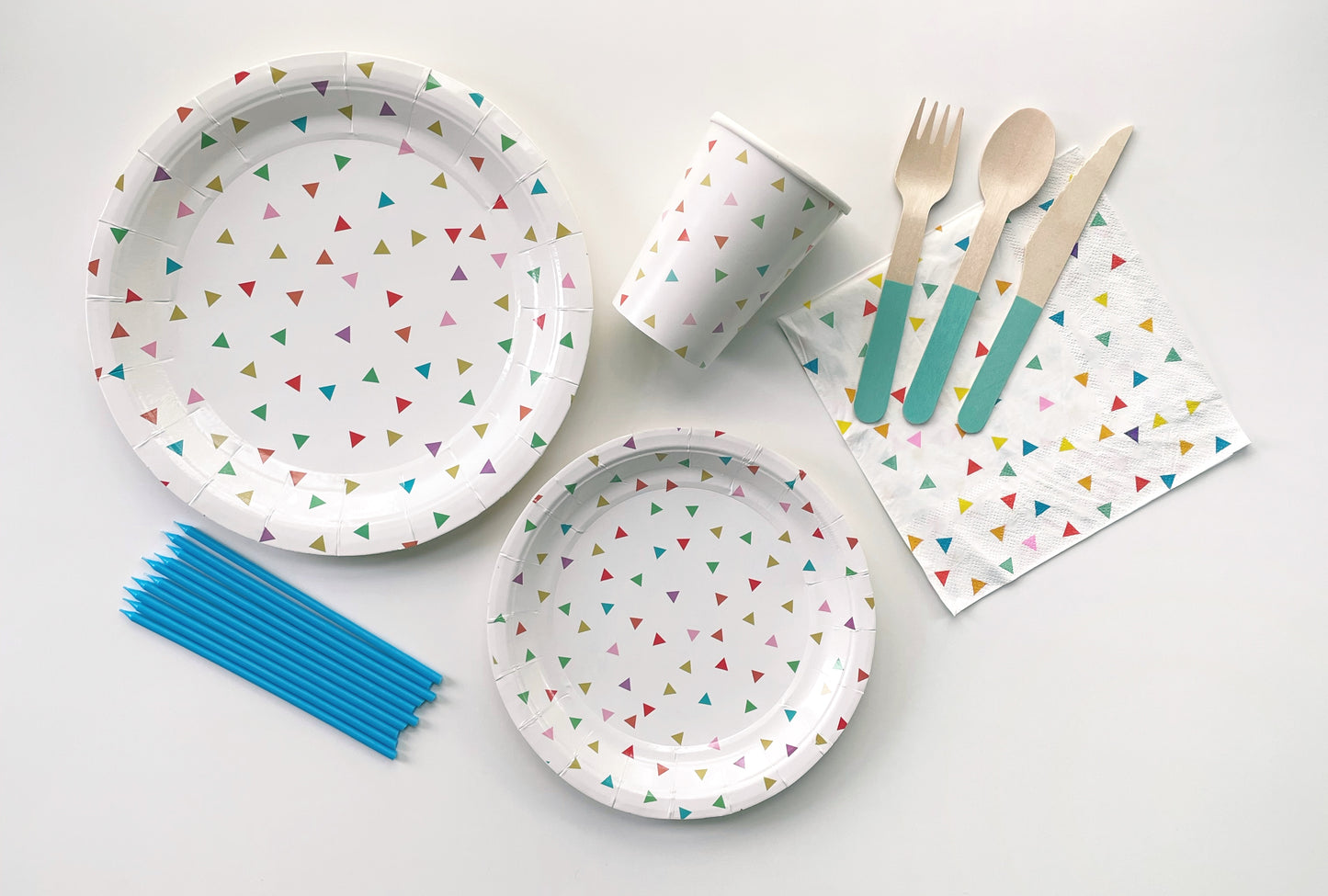 The Tiny Triangle Party Kit including large paper party plates, small paper party plates, paper cups, paper napkins, blue dipped wooden utensils and tall teal birthday candles. The triangle pattern features green, orange, pink, blue and yellow colours.