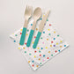 Paper party napkins with a triangle pattern featuring green, orange, pink, blue and yellow colours.  Teal dipped wooden utensils.