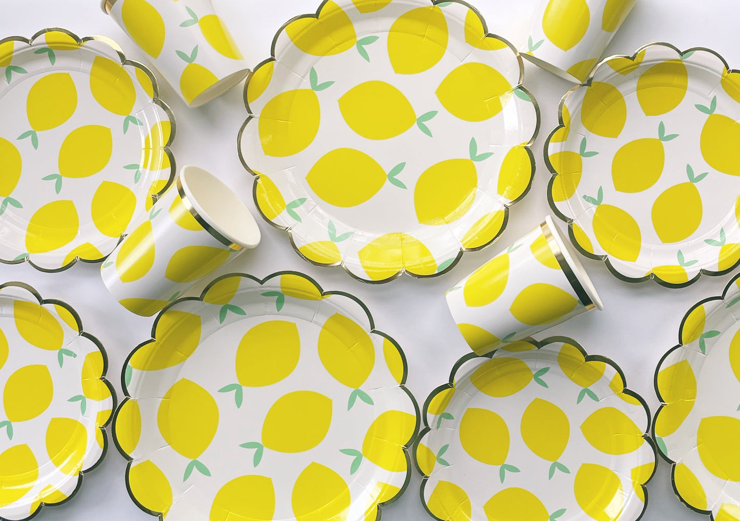 The Lemon Party Kit's paper party plates and cups. The lemon pattern includes yellow, green and white colours. The party plates have gold scalloped edges, and the party cups are trimmed with gold.