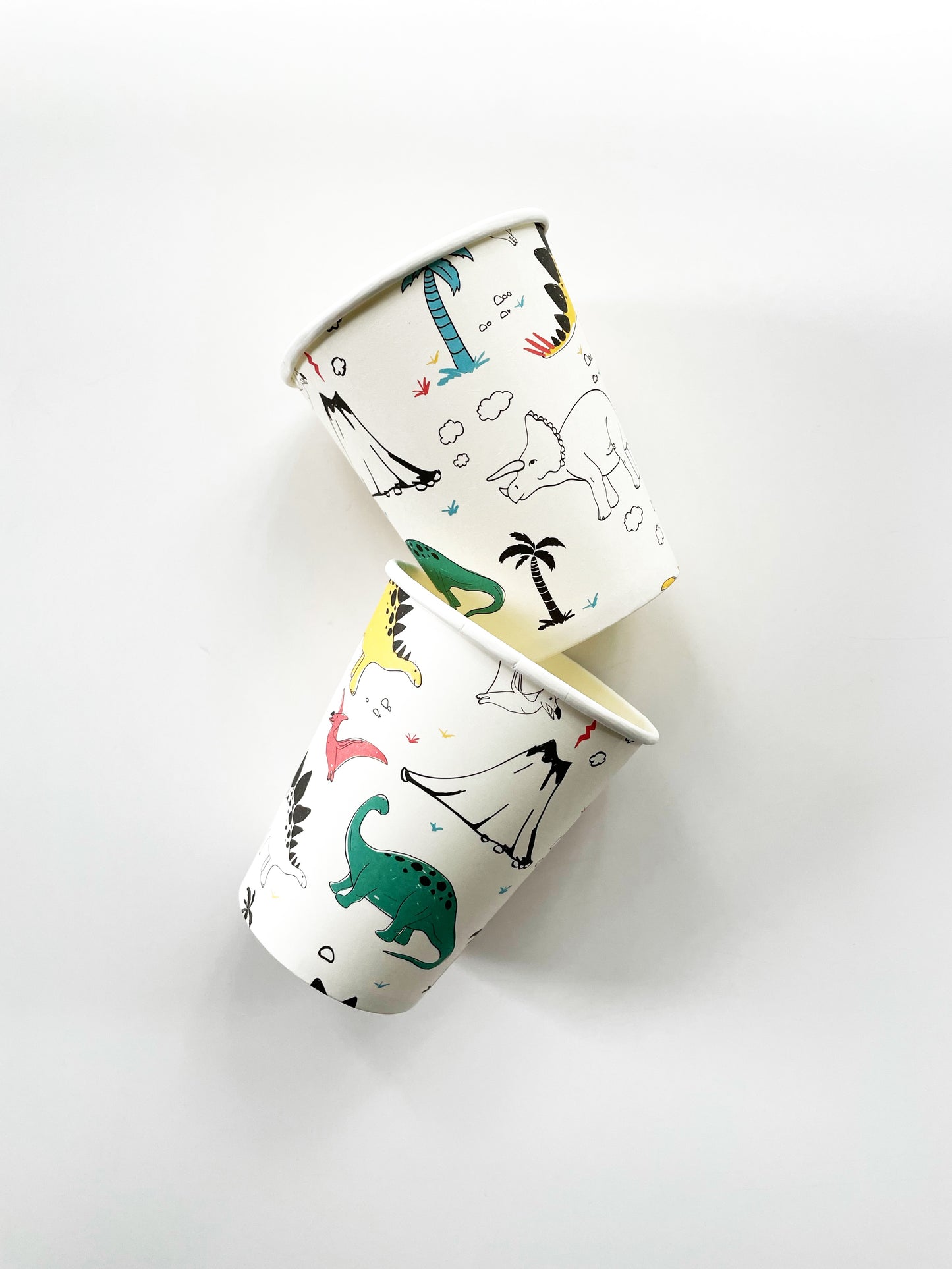 Two paper party cups. The dinosaur pattern features green, blue, yellow, black and red dinosaurs, volcanoes and palm trees.