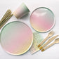  The Ombre Party Kit including large and small circular pink, yellow, green and gold paper party plates, paper cups, paper napkins, gold dipped wooden utensils and tall gold glitter birthday candles.