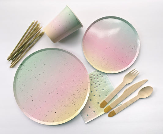  The Ombre Party Kit including large and small circular pink, yellow, green and gold paper party plates, paper cups, paper napkins, gold dipped wooden utensils and tall gold glitter birthday candles.