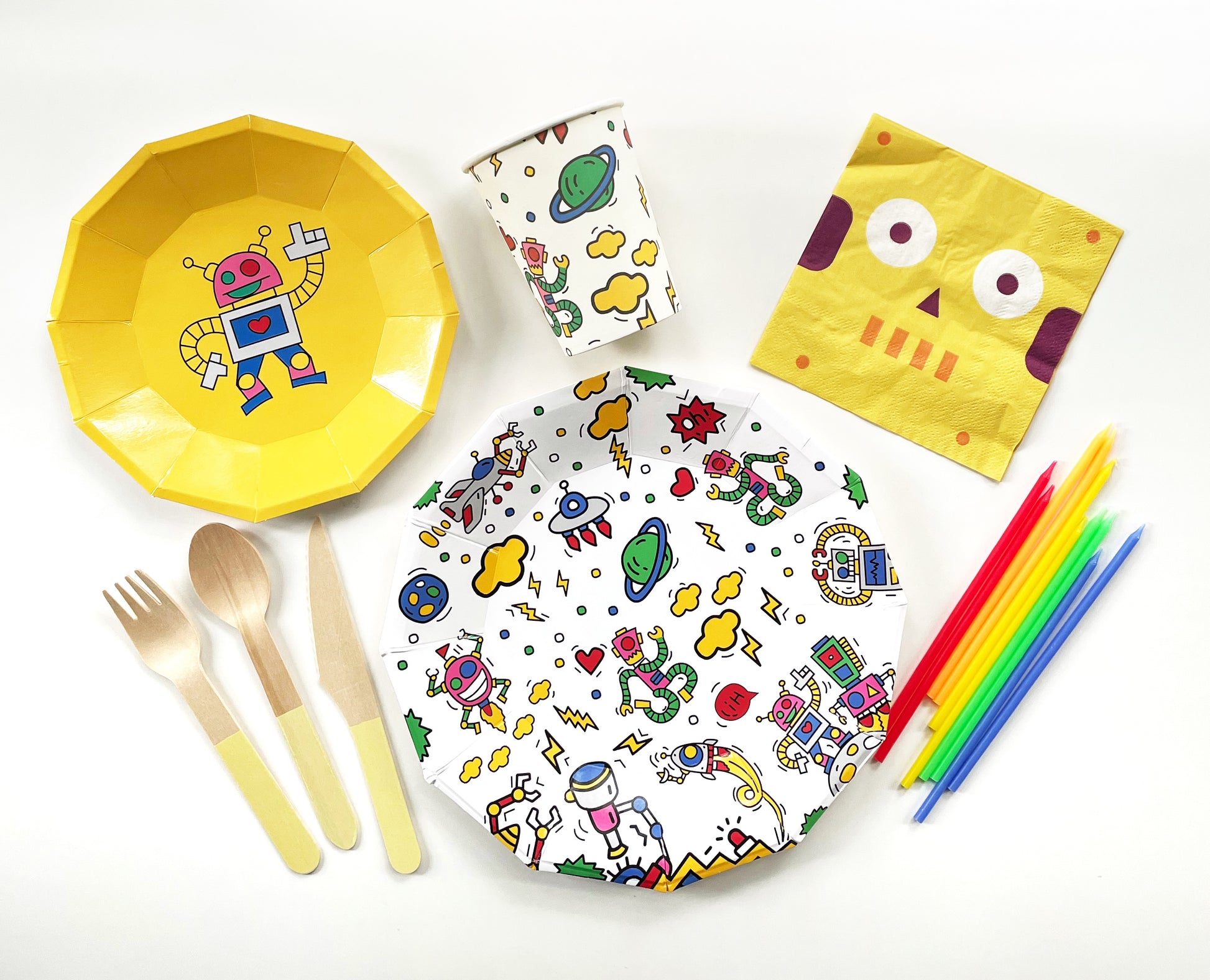 The complete Robot Party Kit including large paper party plates, small yellow paper party plates, paper cups, yellow paper napkins, yellow dipped wooden utensils and tall rainbow birthday candles. The robot pattern includes planets, robots, spaceships and clouds in green, blue, red, yellow and pink colours. The party plates are in the shape of a dodecagon.
