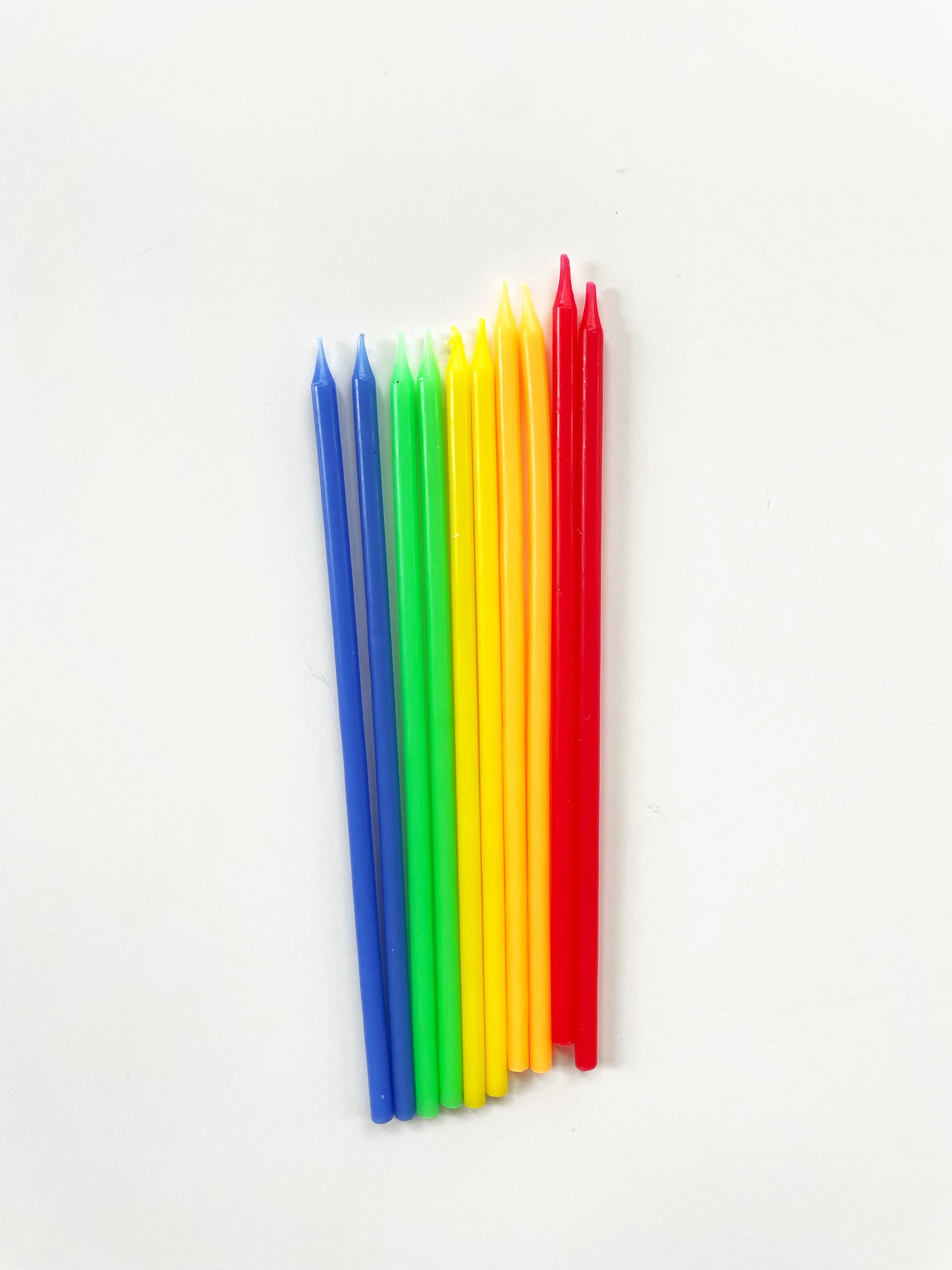 Ten tall rainbow birthday cake candles in yellow, red, green and blue.