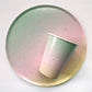 The Ombre Party Kit's large circular pink, yellow, green and gold paper party plates, and party cup.