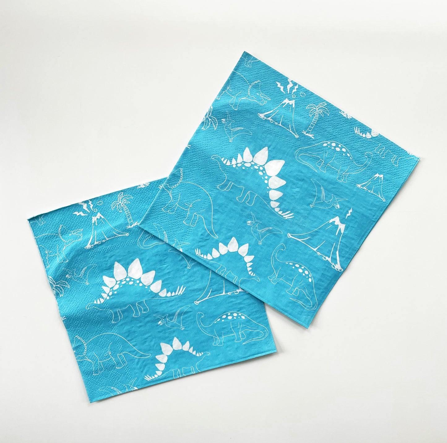 Blue and white paper party napkins. The dinosaur pattern features green, blue, yellow and red dinosaurs, volcanoes and palm trees