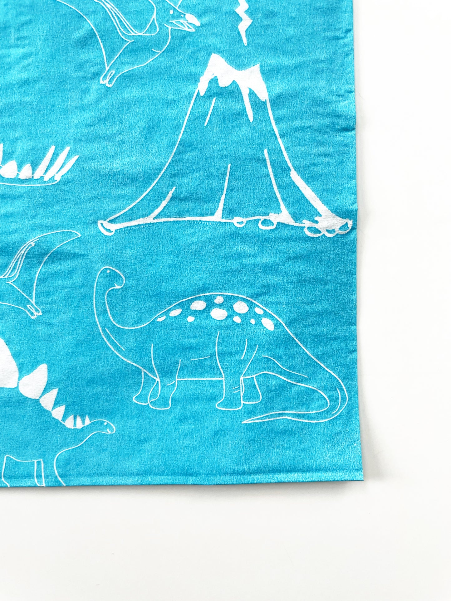 Close up of the blue and white paper party napkins. The dinosaur pattern features green, blue, yellow and red dinosaurs, volcanoes and palm trees