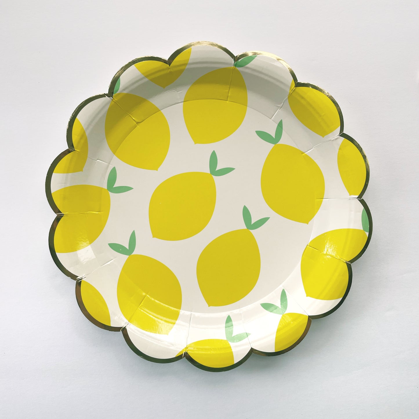 The Lemon Party Kit's paper party plates. The lemon pattern includes yellow, green and white colours. The party plates have gold scalloped edges.